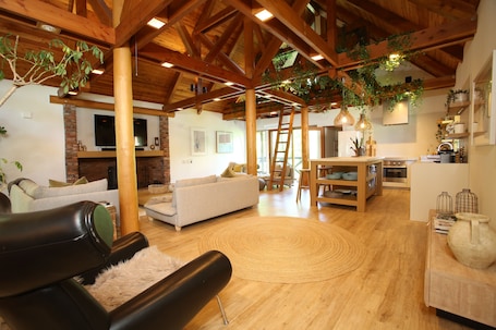 A spacious living area with a high ceiling, wooden beams, a fireplace, sofas, and a dining area with a table and chairs.