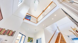 A spacious interior with a high ceiling, a wooden staircase, and a view of the outside through a large window. - StayAU 6BR Deluxe Lakeview Point Cook (Point Cook)