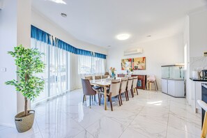 A spacious dining area with a large table and chairs, a potted plant, and a kitchen area with a fish tank. - StayAU 6BR Deluxe Lakeview Point Cook (Point Cook)