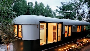 Un vagón de tren con varias ventanas y puertas, rodeado de árboles y luces colgantes.