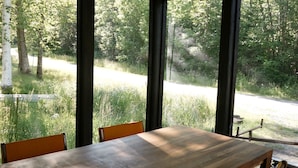 Una mesa de madera para comer con sillas, ventanas amplias y un lámpara colgante.