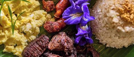 A variety of dishes including rice, sausages, scrambled eggs, and a bowl of soup, all served on a banana leaf.