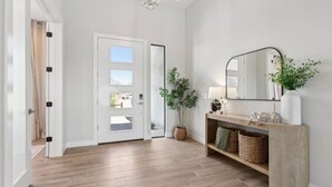 Ein moderner Flur mit Holzboden, einer weißen Tür mit Glasfeldern, einem Spiegel über einer Holzkonsole und einer Topfpflanze.