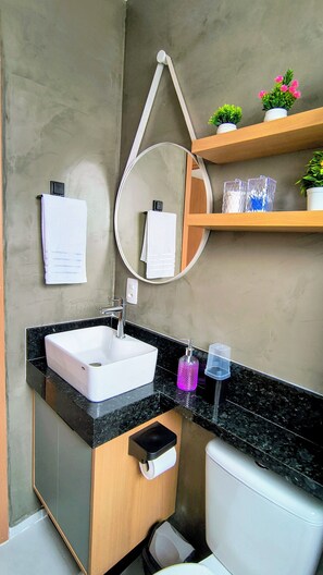 Une salle de bain avec un lavabo blanc, un miroir, un porte-serviettes, des toilettes et une étagère avec des plantes.