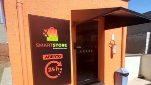 A SMARTSTORE with a 24h service sign, an open door, and a trash bin outside.