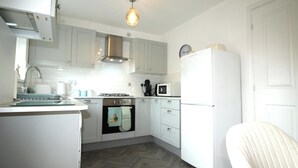 A compact kitchen with white cabinets, a built-in oven, a microwave, and a refrigerator. - House - Sleeps 4 - Pets Ok - Parking (Ashington)