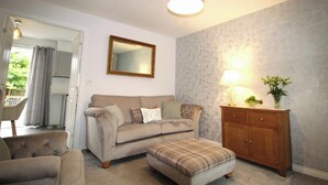 A living room with a sofa, ottoman, wooden cabinet, and a mirror on the wall. - House - Sleeps 4 - Pets Ok - Parking (Ashington)