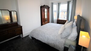 Un dormitorio con una cama grande, un aparador, un espejo y una ventana con cortinas.