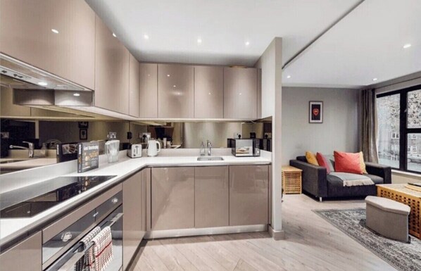 A modern kitchen with a central island, built-in appliances, and a dining area with a sofa and coffee table. - Apartment - Sleeps 2 - Near Tube Stn (London)