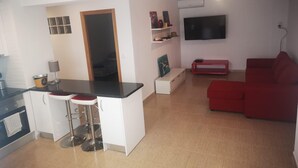 Un espace de vie compact comprenant un coin cuisine, un canapé rouge, un téléviseur et un petit coin repas.