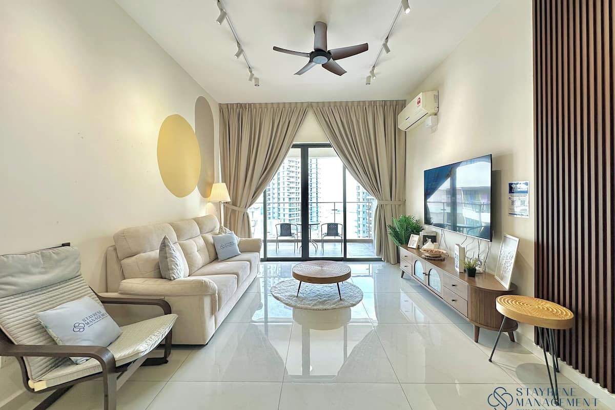A modern living room with a sofa, armchair, and ottoman, a flat-screen TV, and a ceiling fan.