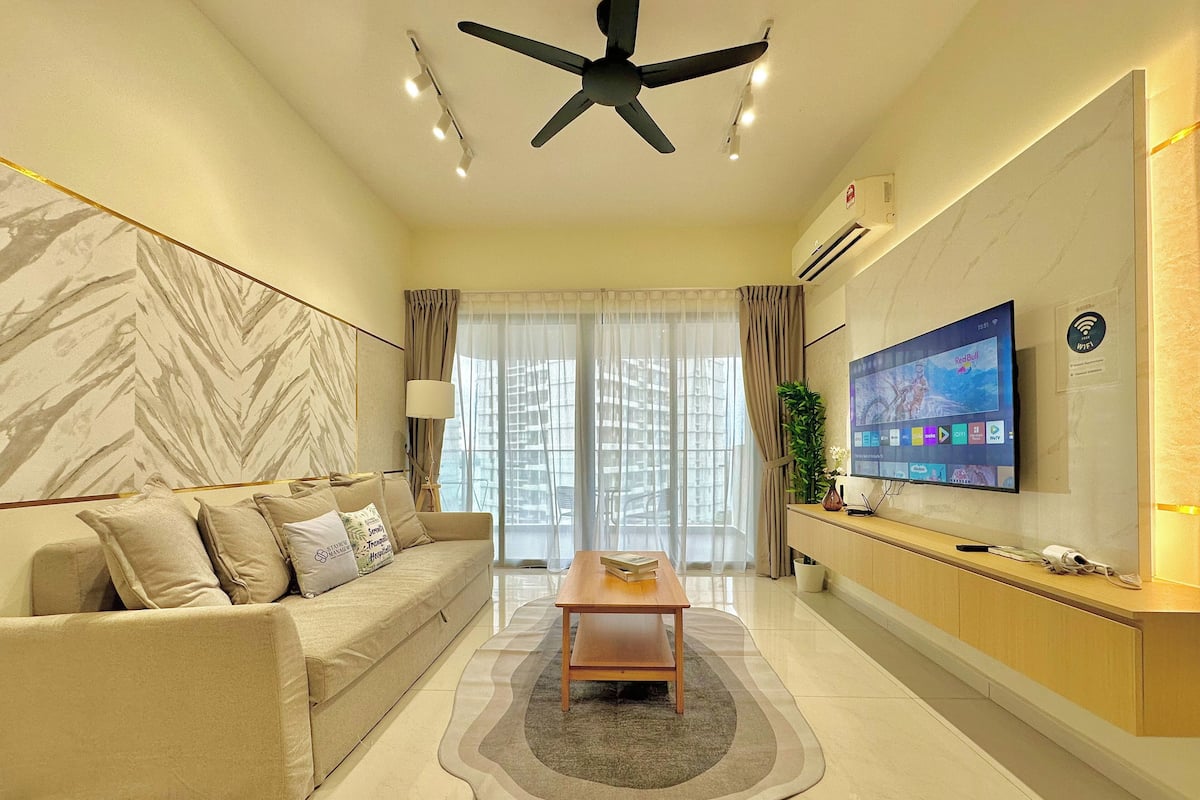 A modern hotel room with a sofa, a coffee table, a TV, and a ceiling fan.