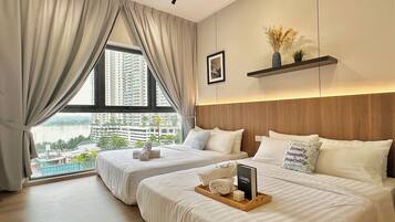 A hotel room with two beds, a large window with curtains, a view of a cityscape, a framed picture on the wall, and a tray with a book and towels.