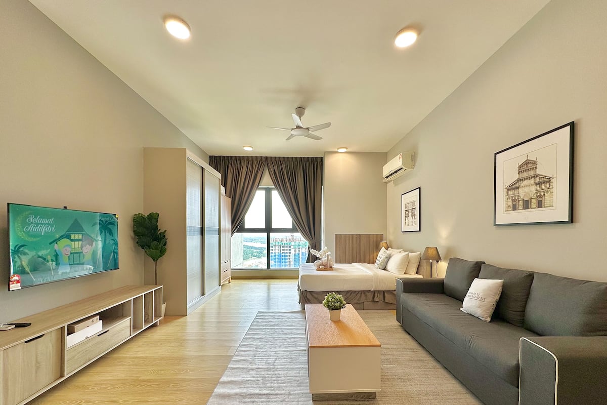 A modern living room with a flat-screen TV, a ceiling fan, a large window with curtains, a sofa, a coffee table, and artwork on the walls.