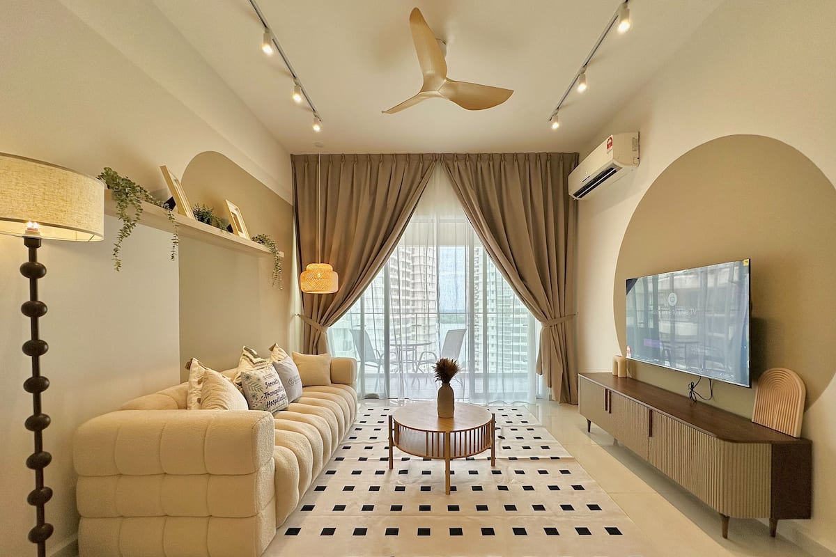 A modern living room with a sofa, a coffee table, a TV, and a large window with curtains.