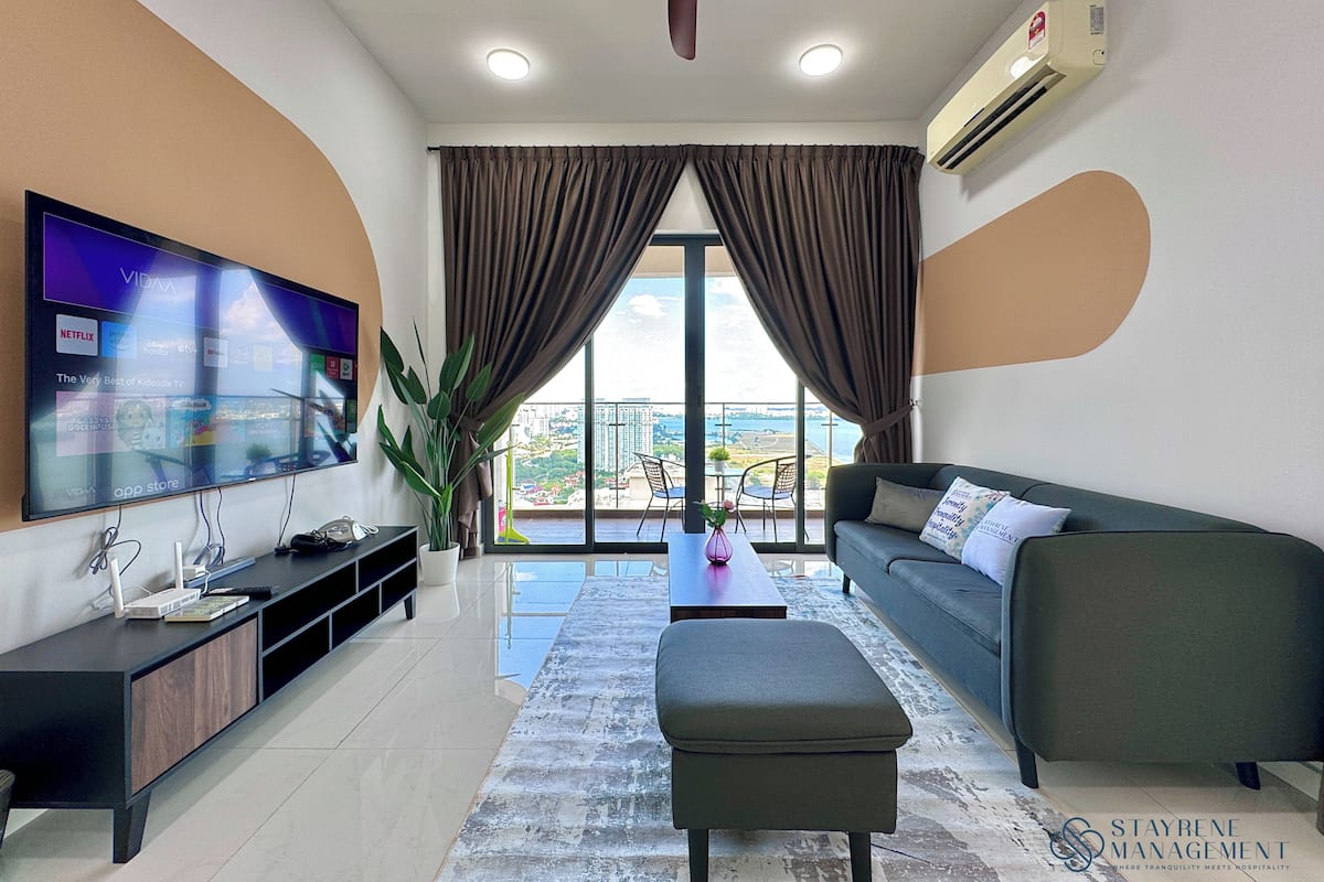A modern living room with a flat-screen TV, a sofa, an ottoman, and a ceiling fan.