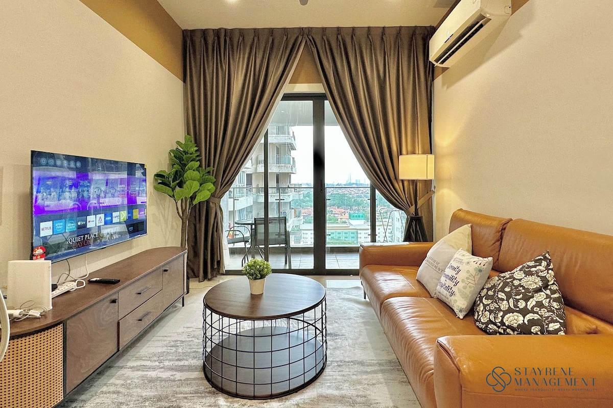 A modern living room with a flat-screen TV, a round coffee table, a sofa, and a view of the city through large windows.