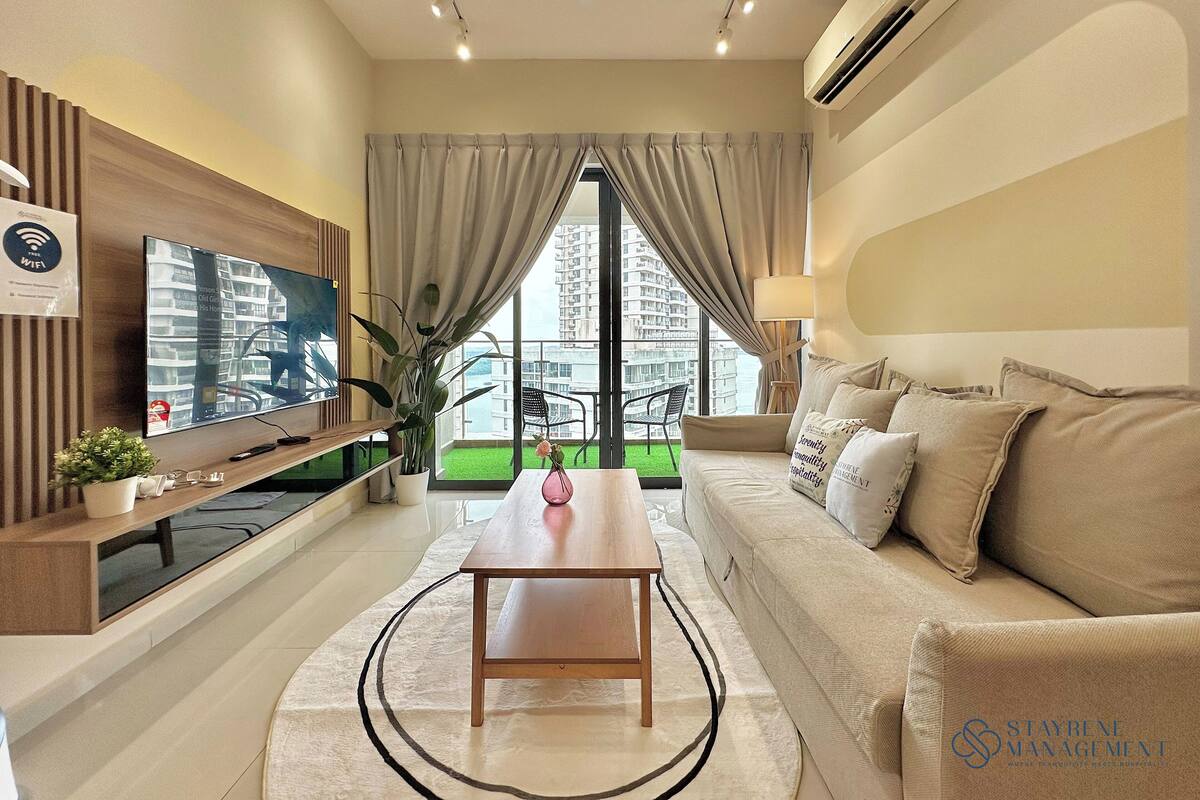 A modern living room with a flat-screen TV, a wooden TV stand, a dining table, a sofa, and a view of a high-rise building through large windows.