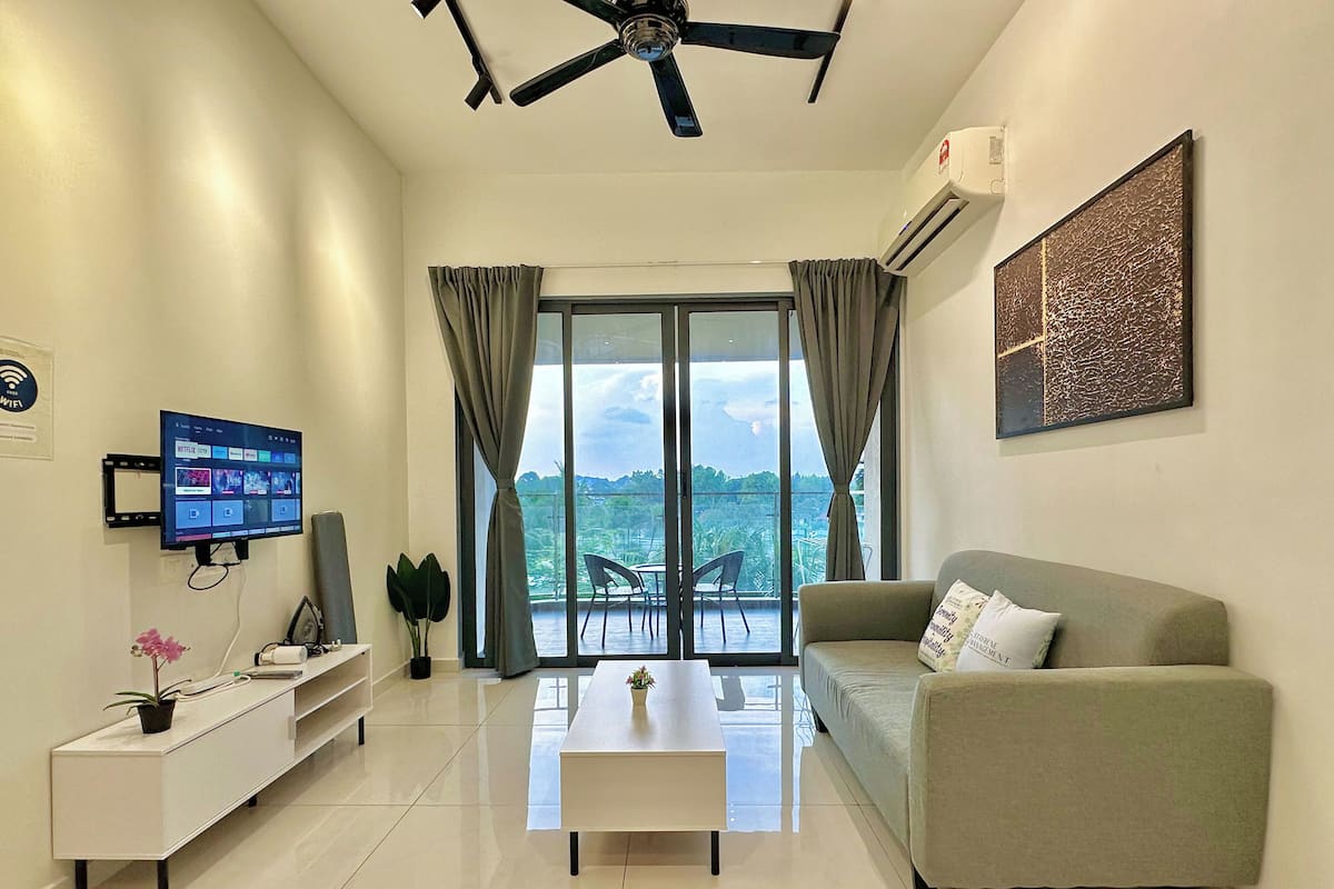 A modern living room with a flat-screen TV, a sofa, a coffee table, and a balcony with a view.
