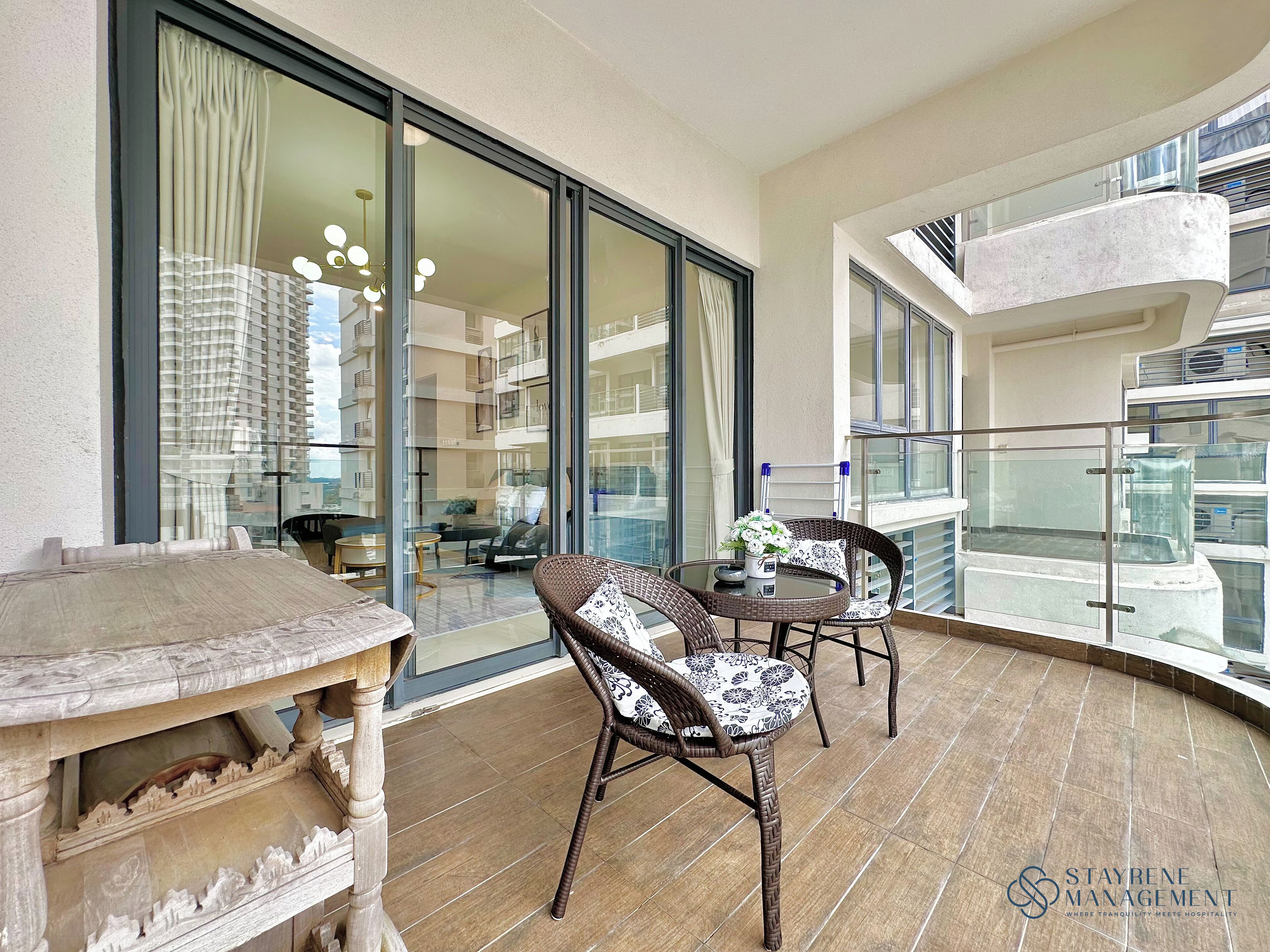 Ein Balkon mit Tisch, zwei Korbstühlen, einer Glasreling und Blick auf ein Hochhaus.