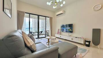 A modern living room with a grey sofa, a flat-screen TV, a ceiling light fixture, and a view of a high-rise building.