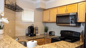 Una cocina con encimeras de granito, electrodomésticos de acero inoxidable, armarios de madera y un ventanal con persianas.