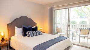 Habitación de hotel con una cama grande, una mesita de noche con lámpara y vistas al balcón exterior.