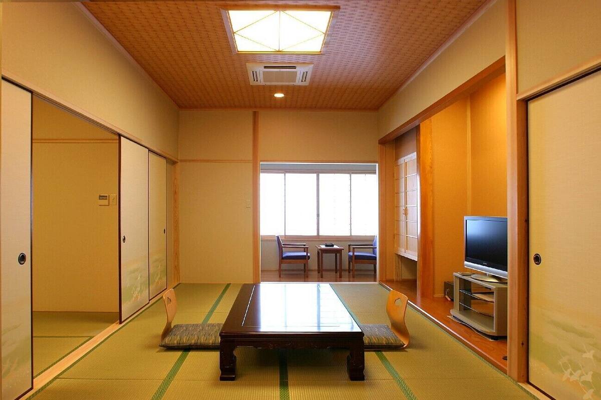 Una habitación japonesa tradicional con suelo de tatami, una mesa baja, puertas correderas y un televisor.