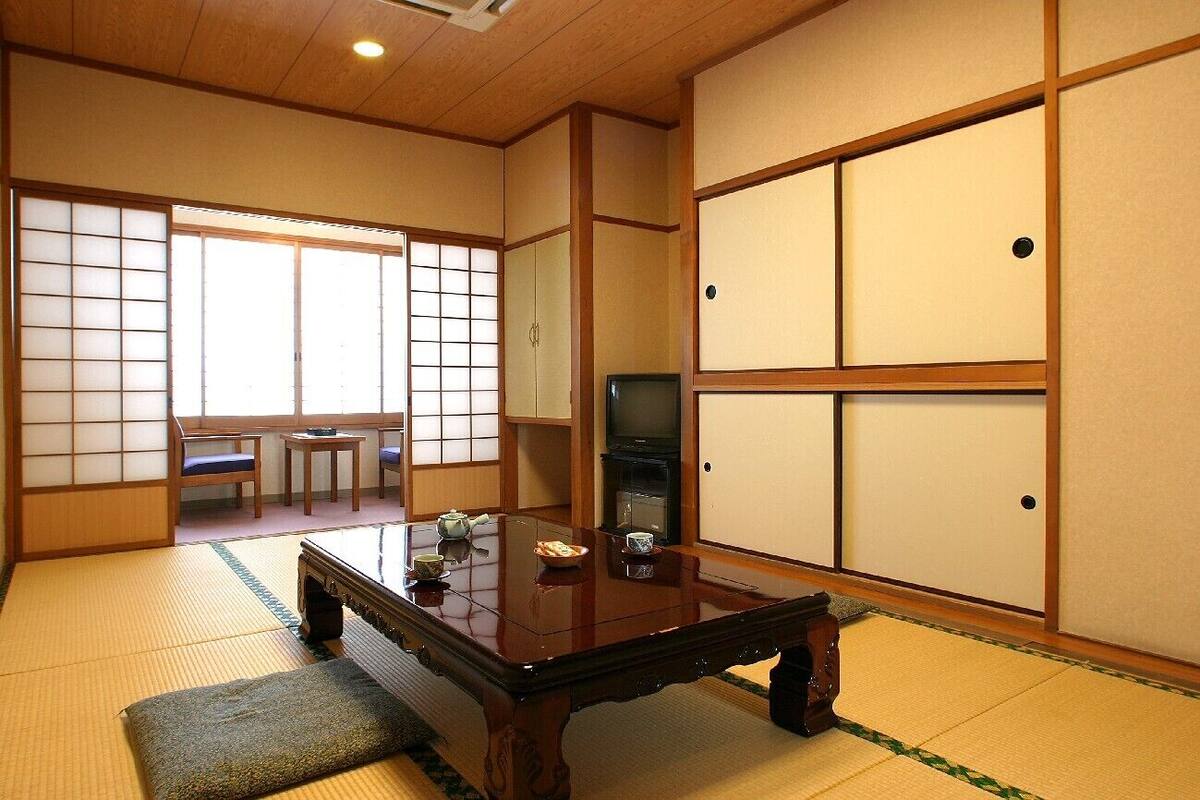 Una habitación japonesa tradicional con suelo de tatami, una mesa de madera baja, un televisor y puertas correderas.