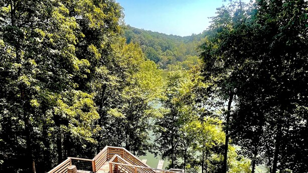 Una terraza con asientos y un brasero, rodeada de árboles y vistas a un lago.