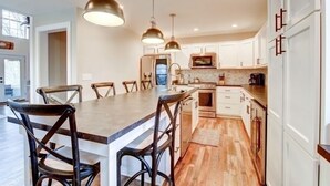 Una cocina moderna con armarios blancos, una isla central con taburetes y iluminación colgante, con vistas al área de estar.