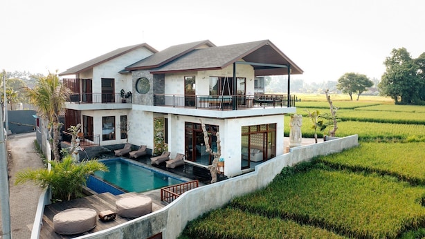 A two-story house with a swimming pool, outdoor seating, and a view of a rice field. - Kari Senja Luxury Villa  (Mas)