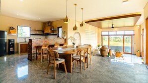 A spacious kitchen with a dining area, featuring a large island, wooden chairs, and pendant lighting. - Kari Senja Luxury Villa  (Mas)