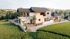 A two-story house with a balcony, a stone facade, and a surrounding garden. - Kari Senja Luxury Villa  (Mas)