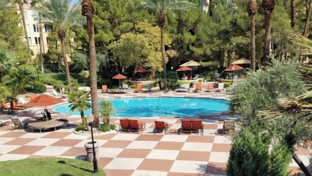 A pool area with checkered flooring, lounge chairs, and palm trees.