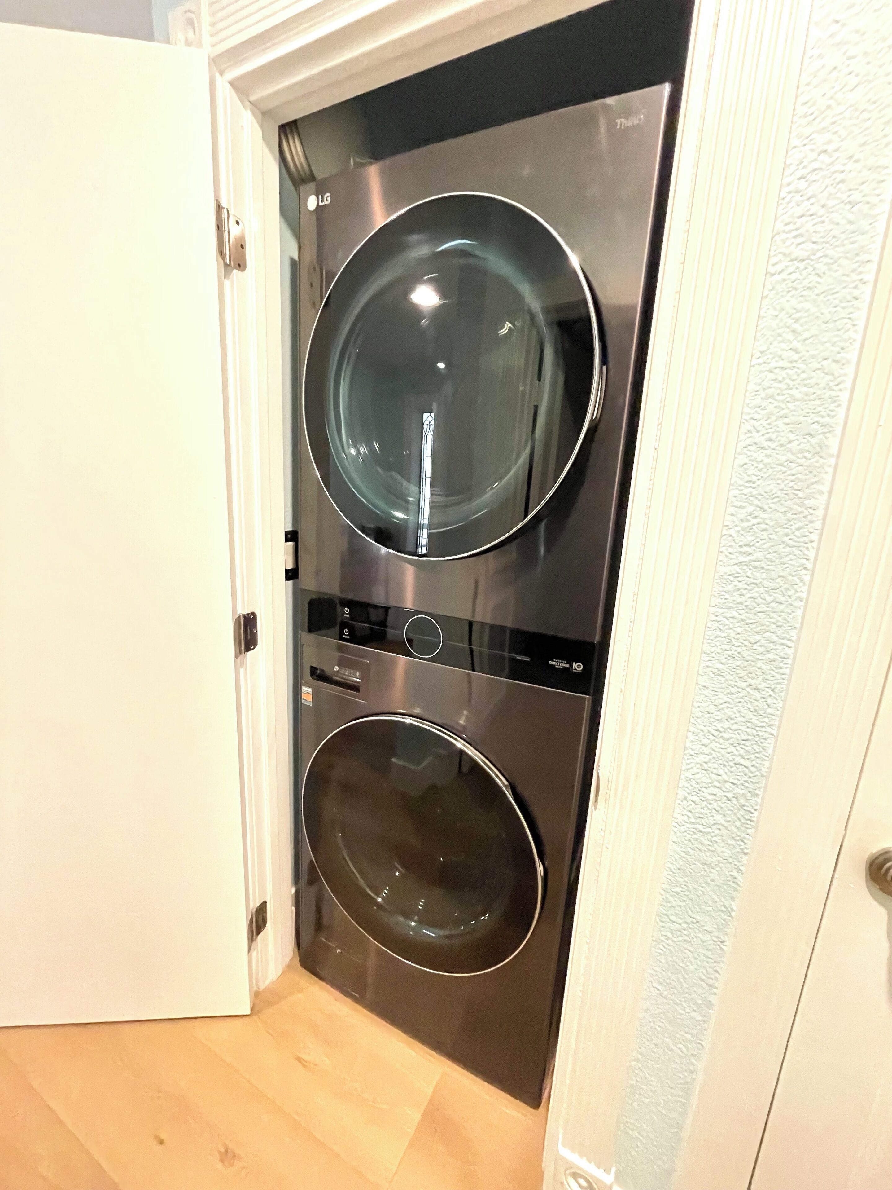 A compact, stainless steel front-loading washer and dryer unit installed in a narrow hallway with a wooden floor.