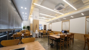A modern dining area with wooden tables and chairs, a digital menu display, and a view through large windows. - Jeonju Hotel Davin (Jeonju)