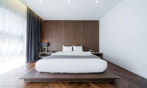 A modern hotel room with a large bed, wooden panel walls, a nightstand with a lamp, and a view of the city through large windows. - Jeonju Hotel Davin (Jeonju)