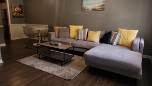 A modern living room with a grey sofa, a coffee table, and a dining area with a glass table and chairs. - Charming Home near Historic Rome (Silver Creek)