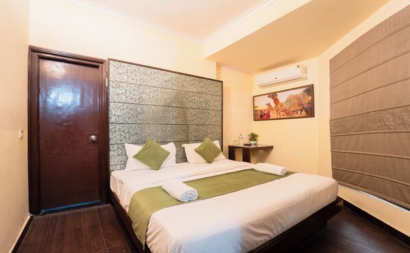 A neatly made bed with white and green bedding, a wooden headboard, and a small bedside table with a plant.
