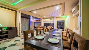 Un restaurant amb una taula de dinar llarga, diverses cadires i una barra amb un cartell de làmpades làmines.