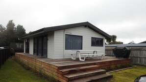 A small, single-story house with a wooden deck and a bench. - Hinenamu Cottage -Two Bedroom and located in a quiet Cul de Sac! (Turangi)