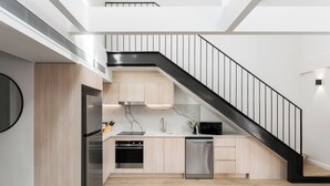 A modern kitchen with a black staircase, stainless steel appliances, and light wood cabinetry. - The Henrietta Apartments by Urban Rest (Double Bay)