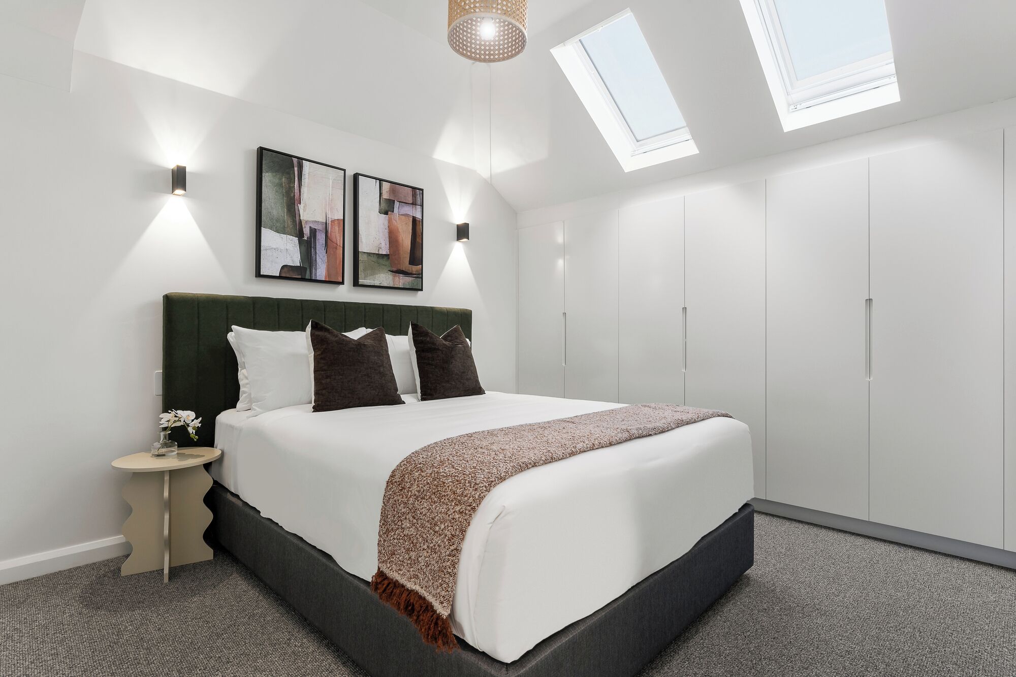 Une chambre à coucher moderne avec un lit, une table de chevet, des œuvres d’art et des fenêtres de toit.