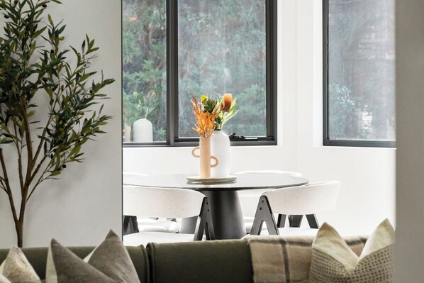 A dining area with a round table, white chairs, and a vase with flowers. - The Henrietta Apartments by Urban Rest (Double Bay)