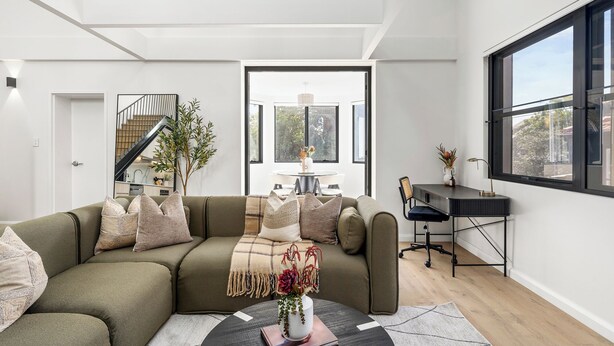 A modern living room with a sofa, coffee table, and a desk with a chair. There is a staircase leading to an upper level. - The Henrietta Apartments by Urban Rest (Double Bay)