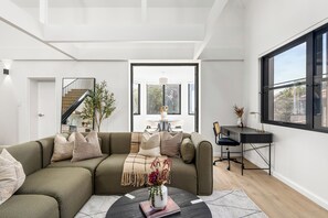 A modern living room with a sofa, coffee table, and a desk with a chair. There is a staircase leading to an upper level. - The Henrietta Apartments by Urban Rest (Double Bay)