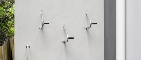 Pared con tres pomos metálicos, probablemente para una puerta corredera o portón, frente a una pared lisa con una valla de madera y vegetación al fondo.