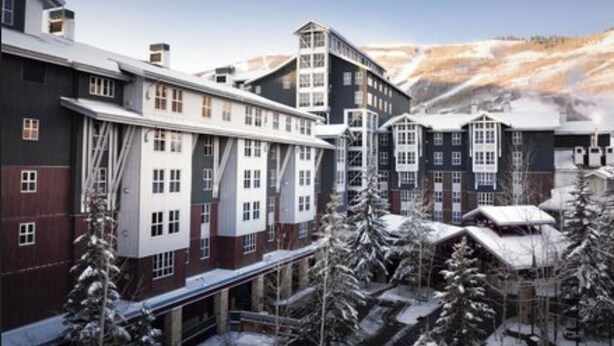 Un hotel con varias construcciones, incluyendo un edificio de esquina destacado con fachada blanca y roja, y una edificación más pequeña con fachada oscura.