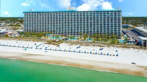 Un hotel grande de diseño moderno, cerca de una playa con numerosas sombrillas y un área de piscina.